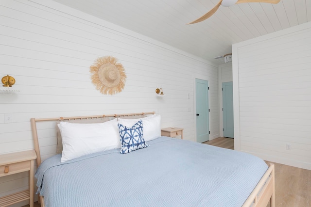 bedroom with light hardwood / wood-style flooring, ceiling fan, and wood walls