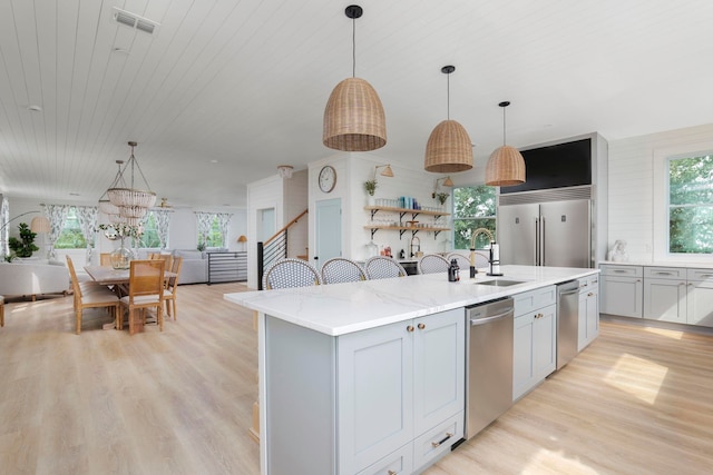 kitchen featuring sink, an island with sink, light hardwood / wood-style floors, decorative light fixtures, and appliances with stainless steel finishes