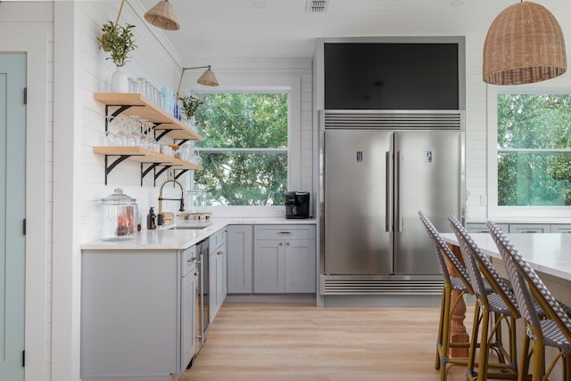 kitchen featuring gray cabinetry, sink, light stone counters, light hardwood / wood-style flooring, and appliances with stainless steel finishes