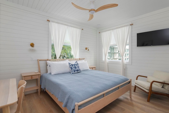 bedroom featuring hardwood / wood-style flooring, ceiling fan, and wooden walls