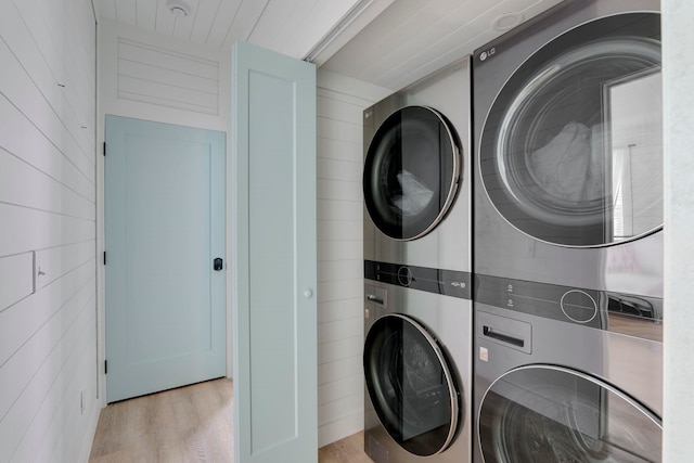 washroom with stacked washer / dryer, wood walls, and light hardwood / wood-style flooring