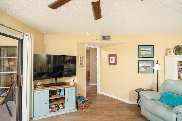 living room featuring ceiling fan, light hardwood / wood-style flooring, and a textured ceiling