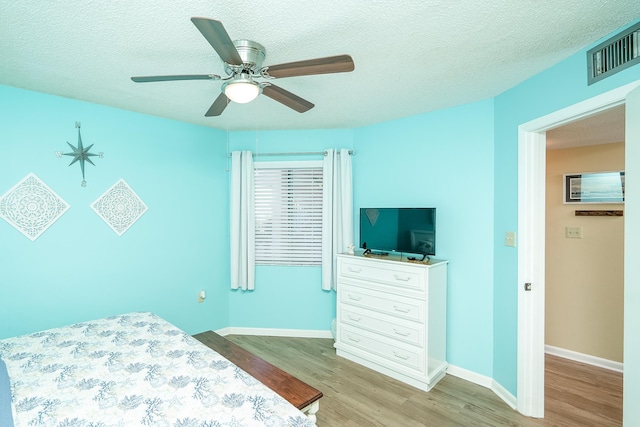 bedroom with ceiling fan, light wood-type flooring, and a textured ceiling