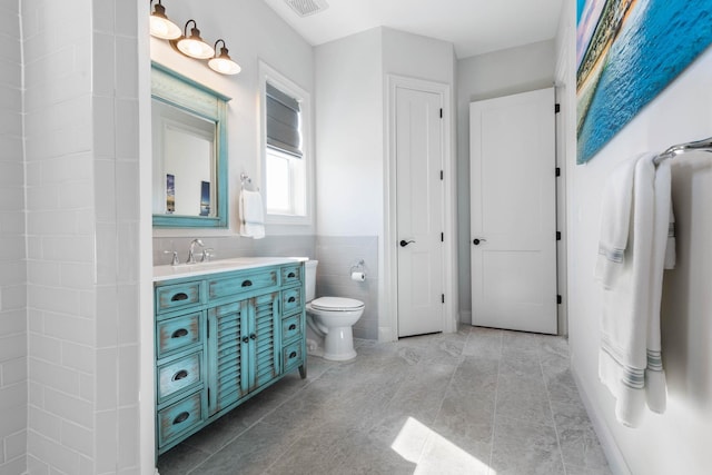 bathroom featuring toilet, tile patterned flooring, tile walls, and vanity