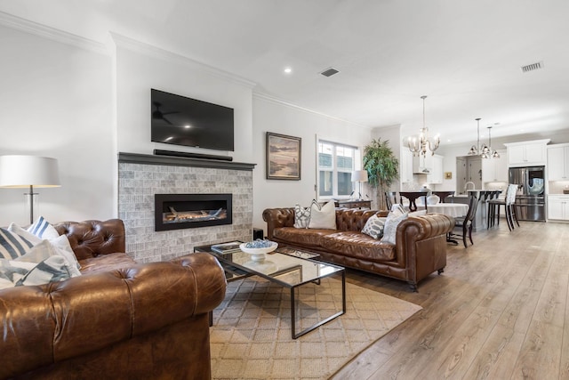 living room with a chandelier, wood-type flooring, ornamental molding, and a tiled fireplace