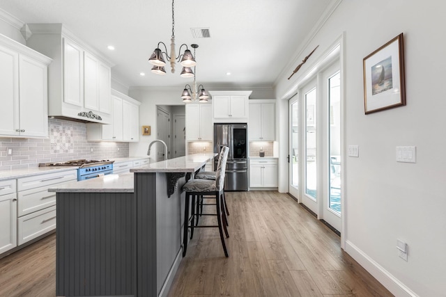 kitchen with light stone countertops, white cabinets, appliances with stainless steel finishes, hanging light fixtures, and a kitchen island with sink