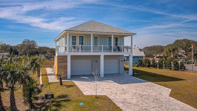 beach home featuring an attached garage, decorative driveway, a front yard, and board and batten siding