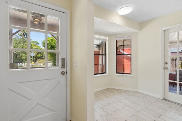doorway featuring a wealth of natural light, baseboards, a textured ceiling, and light wood-style flooring