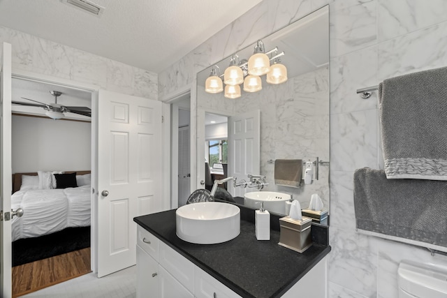 bathroom featuring vanity, ceiling fan, toilet, a textured ceiling, and tile walls