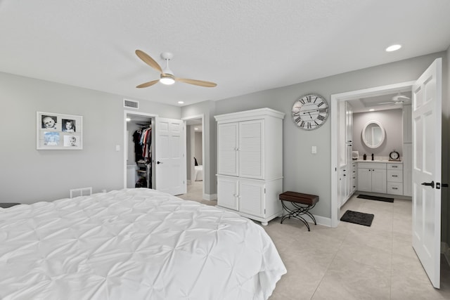 tiled bedroom with a walk in closet, ensuite bath, a textured ceiling, ceiling fan, and a closet