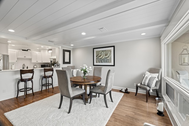 dining area with hardwood / wood-style flooring, beam ceiling, and ornamental molding