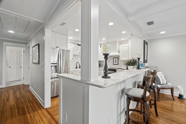 kitchen with kitchen peninsula, stainless steel fridge, a kitchen bar, wood-type flooring, and white cabinetry