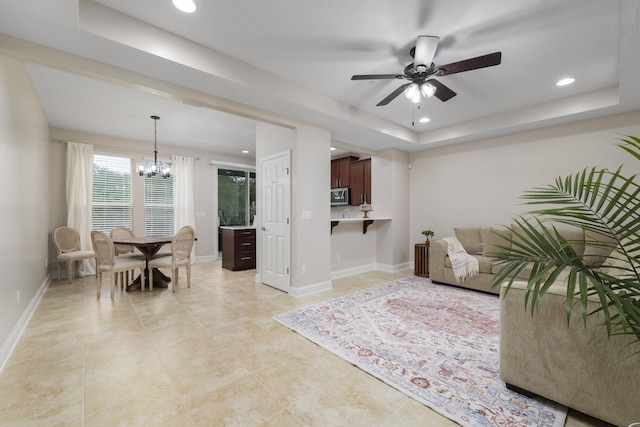 tiled living room featuring a tray ceiling and ceiling fan with notable chandelier