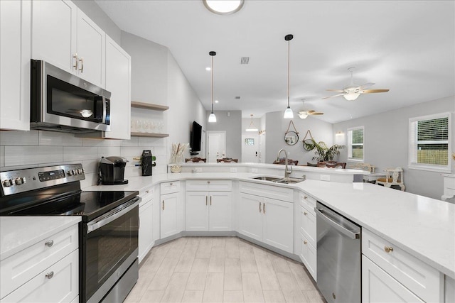 kitchen with stainless steel appliances, light countertops, hanging light fixtures, white cabinets, and a sink