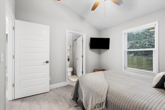 bedroom featuring light wood finished floors, baseboards, a ceiling fan, lofted ceiling, and ensuite bath