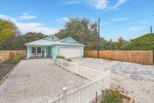 ranch-style house with metal roof, concrete driveway, a fenced front yard, and a garage