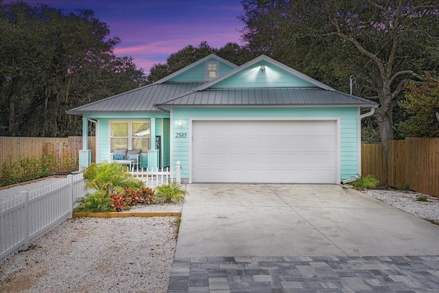 view of front of property featuring driveway, an attached garage, fence, and metal roof