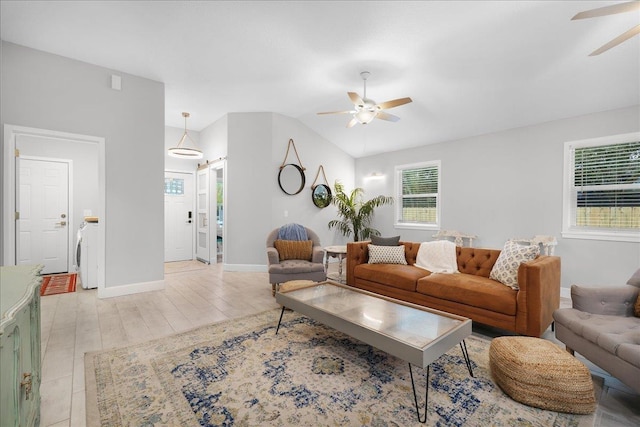 living area featuring washer / dryer, baseboards, lofted ceiling, ceiling fan, and light wood-style flooring