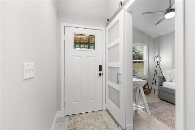 interior space with a barn door, baseboards, a ceiling fan, lofted ceiling, and light wood-type flooring