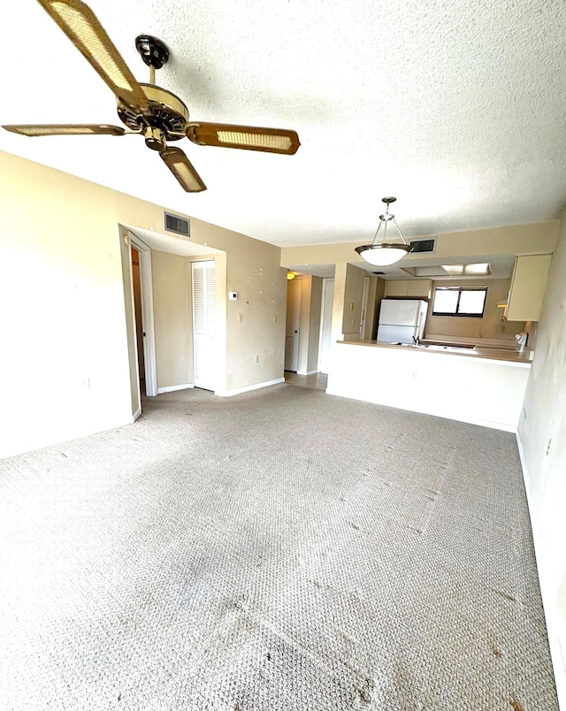 unfurnished living room featuring carpet, visible vents, baseboards, and ceiling fan