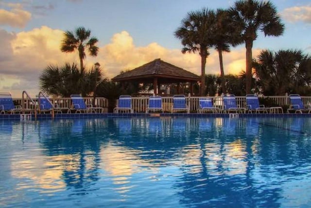 pool at dusk with a community pool, fence, and a gazebo