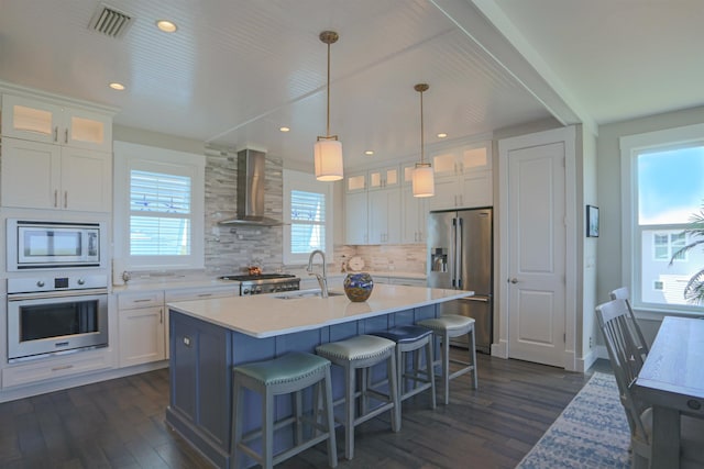 kitchen with appliances with stainless steel finishes, white cabinetry, wall chimney exhaust hood, and sink