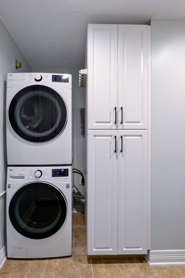 laundry area with cabinets, light tile patterned floors, and stacked washer / dryer