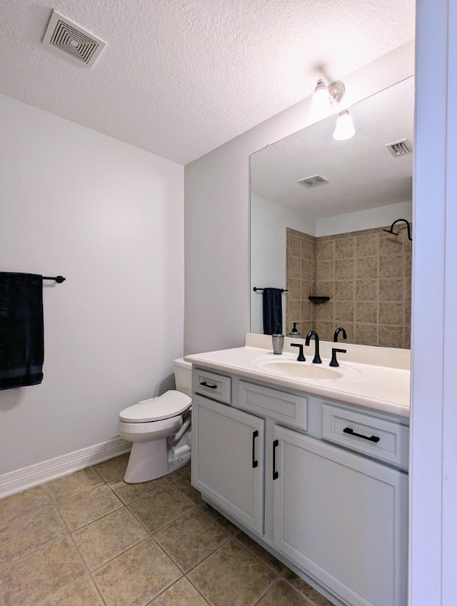 bathroom with tile patterned floors, vanity, a textured ceiling, tiled shower, and toilet