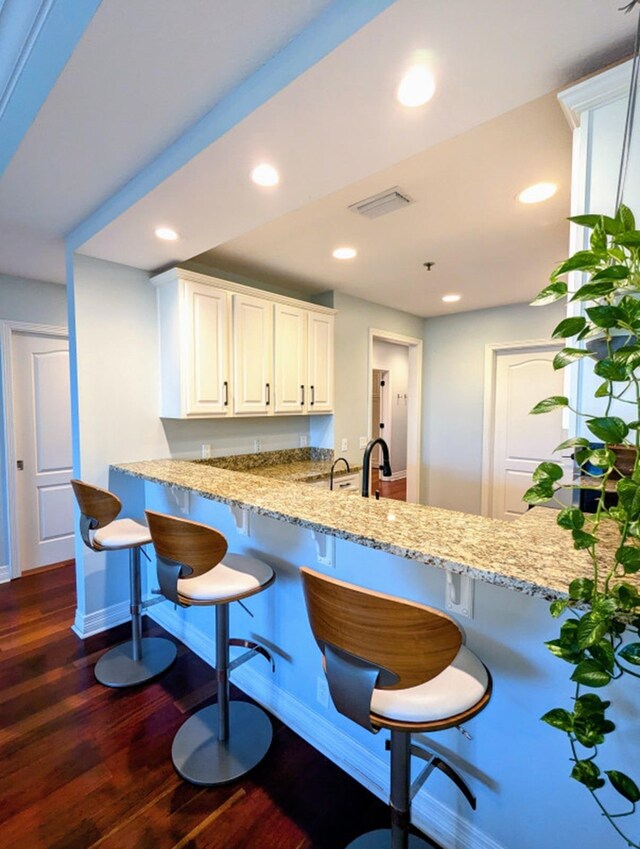 kitchen with kitchen peninsula, dark hardwood / wood-style floors, light stone counters, white cabinetry, and a breakfast bar area