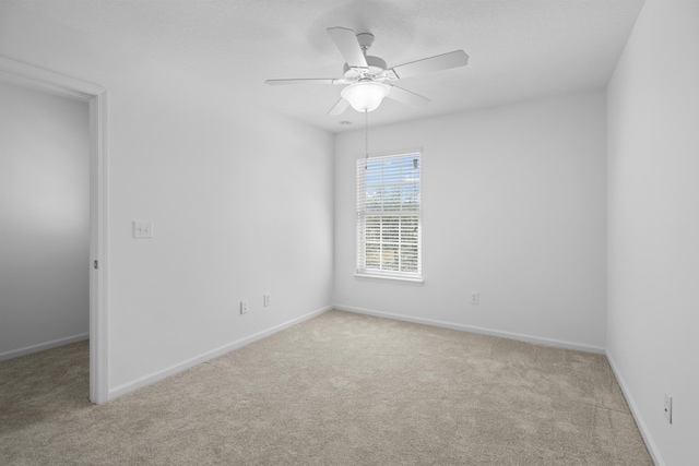 spare room featuring light colored carpet, baseboards, and ceiling fan