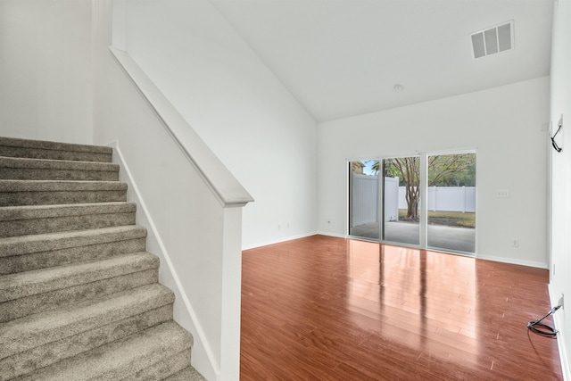 stairway featuring high vaulted ceiling, wood finished floors, visible vents, and baseboards