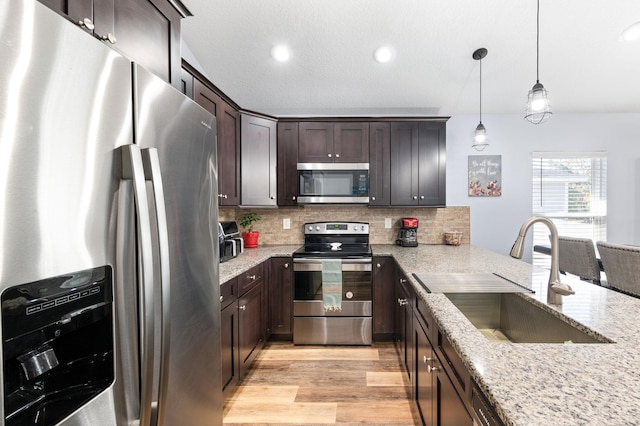 kitchen with light stone countertops, tasteful backsplash, hanging light fixtures, sink, and stainless steel appliances