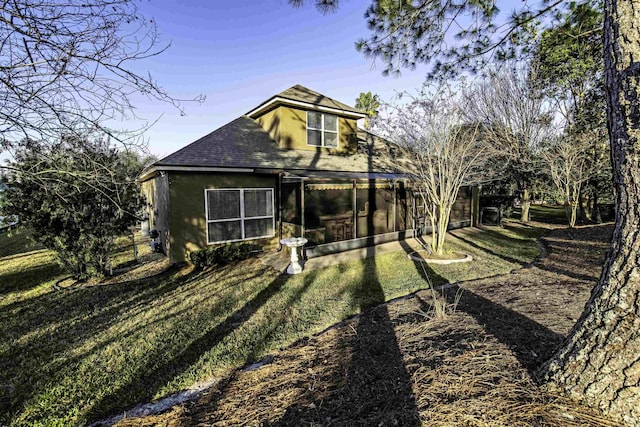 rear view of house with a shingled roof, a sunroom, a yard, and stucco siding