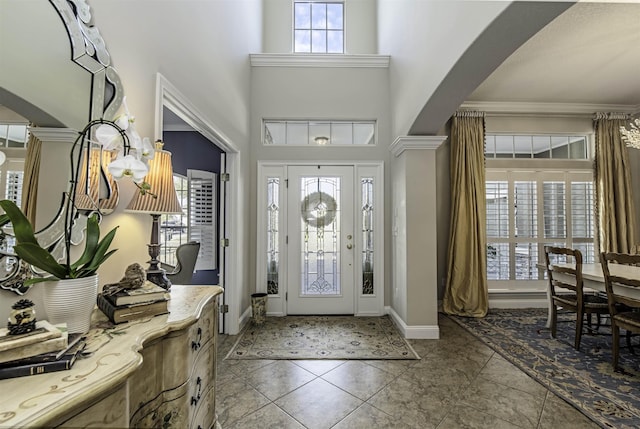 tiled foyer with arched walkways, a high ceiling, baseboards, ornamental molding, and decorative columns