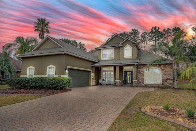 view of front of home featuring decorative driveway, a yard, stucco siding, an attached garage, and stone siding