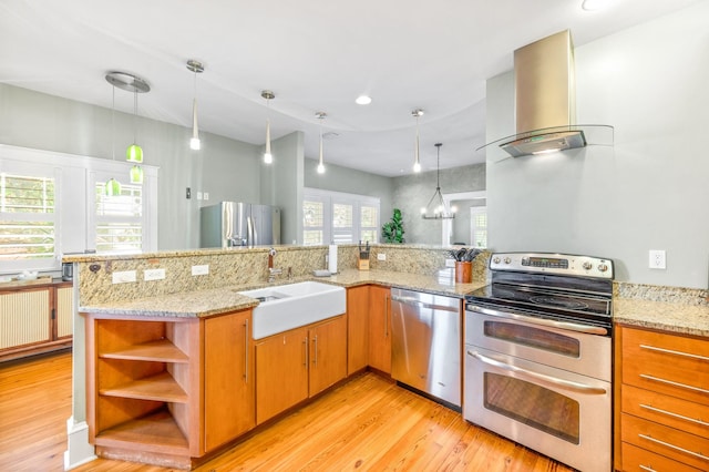 kitchen featuring appliances with stainless steel finishes, light stone counters, wall chimney range hood, sink, and light hardwood / wood-style floors