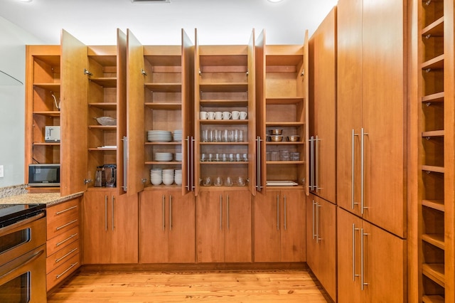 room details with light stone counters, light wood-type flooring, and stainless steel appliances