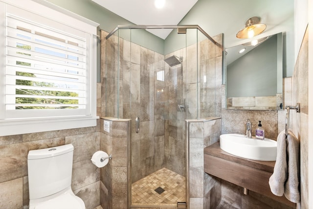 bathroom featuring vanity, toilet, a shower with shower door, and tile walls