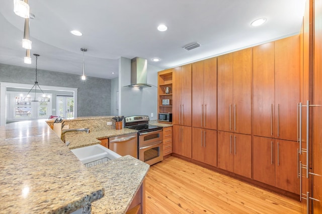 kitchen featuring pendant lighting, wall chimney range hood, sink, light wood-type flooring, and appliances with stainless steel finishes