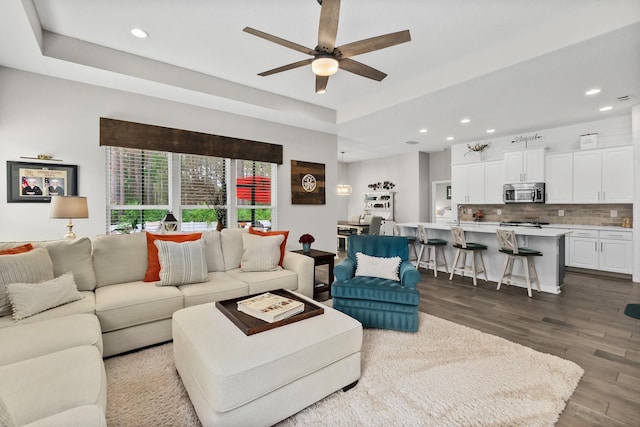 living area with recessed lighting, a raised ceiling, ceiling fan, and wood finished floors