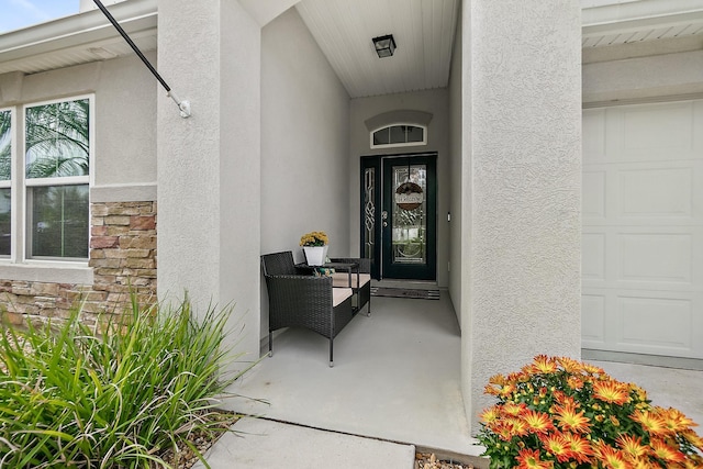 entrance to property with stucco siding, stone siding, and a garage