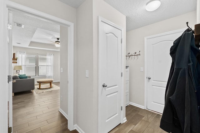 interior space featuring baseboards, visible vents, wood finish floors, a textured ceiling, and a raised ceiling