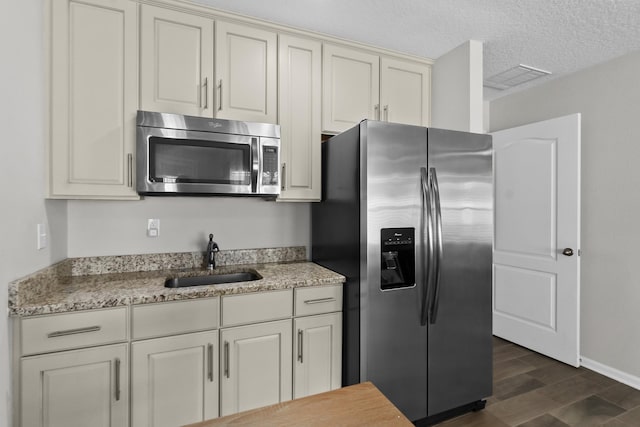 kitchen with sink, dark wood-type flooring, appliances with stainless steel finishes, light stone counters, and a textured ceiling