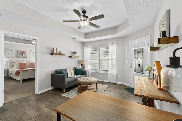 living room with ceiling fan, a tray ceiling, and a textured ceiling