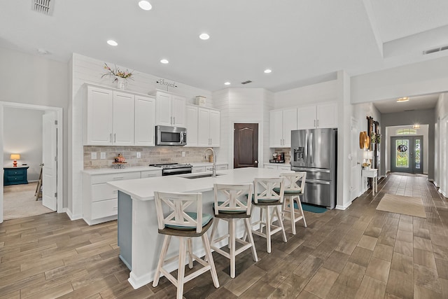 kitchen featuring visible vents, backsplash, a sink, stainless steel appliances, and a kitchen island with sink