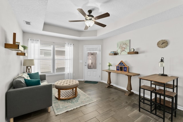 living area with ceiling fan, dark wood-type flooring, a textured ceiling, and a tray ceiling