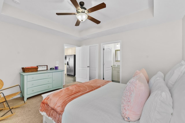 bedroom featuring connected bathroom, ceiling fan, light colored carpet, stainless steel refrigerator with ice dispenser, and a raised ceiling