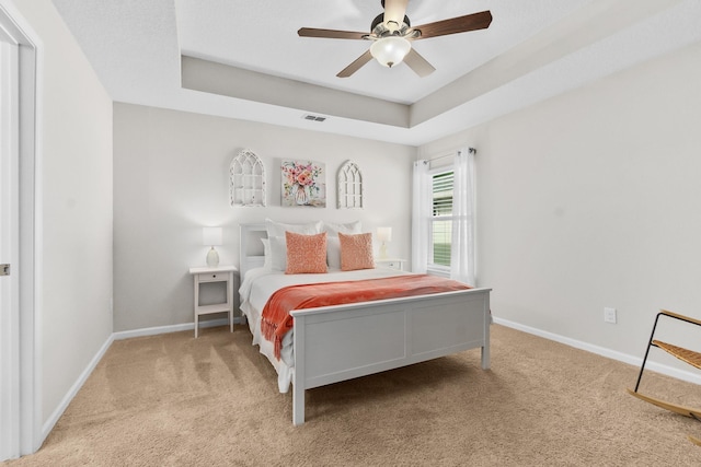 bedroom with light colored carpet, ceiling fan, and a tray ceiling