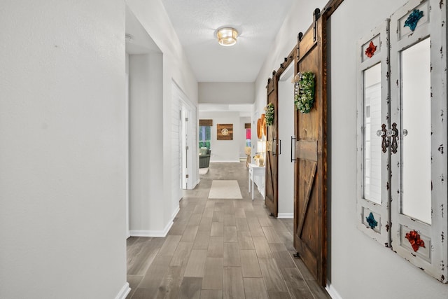 corridor with a barn door, baseboards, a textured ceiling, and wood finished floors