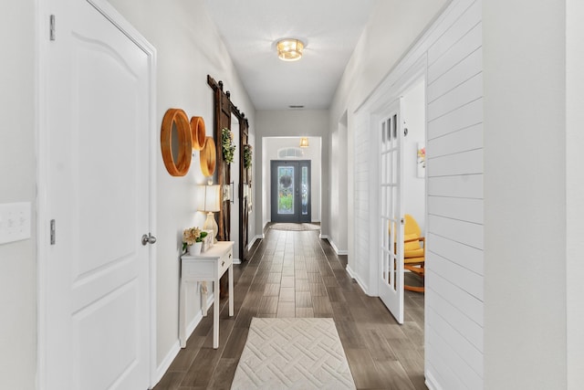 corridor featuring a barn door, baseboards, french doors, and dark wood finished floors